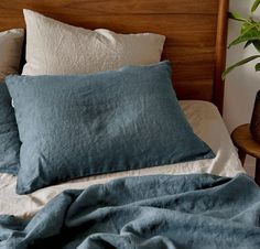 an unmade bed with blue linens and pillows on it, next to a potted plant