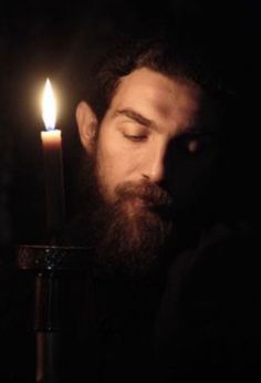 a bearded man holding a lit candle in his hand