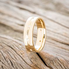 a yellow gold wedding ring with diamonds on it sitting on a piece of drift wood