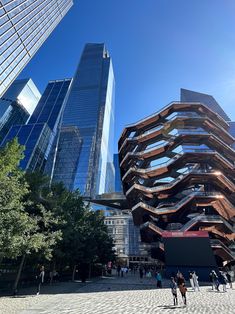 people are walking around in front of some very tall buildings on a sunny day with blue skies