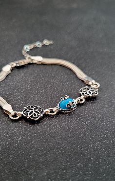 a silver bracelet with blue beads and charms on it's sides, sitting on a black surface