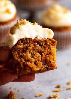 a hand holding up a cupcake with white frosting