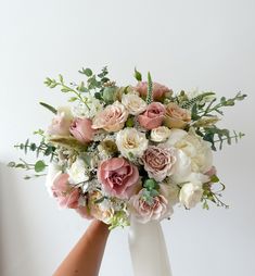 a bouquet of flowers is being held up by someone's hand in front of a white wall