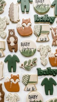 baby shower cookies are arranged on a white tablecloth with green and brown onesuits