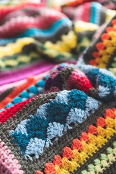 a multicolored crocheted blanket laying on top of a bed covered in blankets