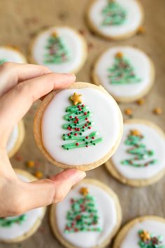 a person holding a decorated christmas tree cookie in front of some cookies on a table