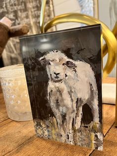 a painting of a sheep on a wooden table next to a glass vase and candle holder