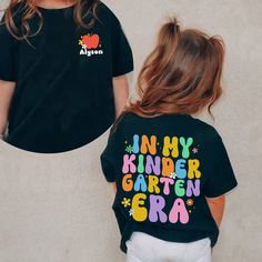 In My Kindergarten Era Shirt, Custom Kindergarten Shirt, First Day Of School, Back To School Shirt, Hello School Shirt, 1st Grade Tee Note: For Different Color From Colors List Please "Message us or leave a note" MATERIAL UNISEX T-SHIRT - Medium fabric (5.3 oz/yd² (180 g/m - Classic fit - Runs true to size - 100% cotton (fiber content may vary for different colors) - Tear-away label UNISEX SIZING CHART Small: Length 28" - Width 18" (4-6) Medium: Length 29" - Width 20" (6-10) Large: Length 30" - Width 22" (10-14) XL: Length 31" - Width 24" (14-18) 2XL: Length 32" - Width 26" (18-20) 3XL: Length 33" - Width 28" (20-22) All measurements are approximations. Shirts may be within 1" of the dimensions listed The shirts were measured laying on a flat surface, side to side and top to bottom. HOW TO Kindergarten Shirts For Kids First Day, First Day Of School Shirts Kids, First Day Of Pre K Shirt, Cute T-shirt With Name Print For Teacher Appreciation, Customizable Cute Tops For School, Cute Customizable Tops For School, Cute Multicolor Shirt With Letter Print, Playful Personalized Cotton Tops, Personalized Cute Cotton Shirt