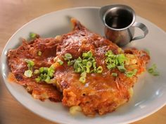 a white plate topped with lasagna covered in sauce and green onions next to a cup