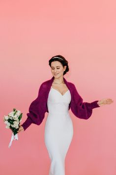 a woman in a white dress and purple cardigan is holding a bouquet of flowers