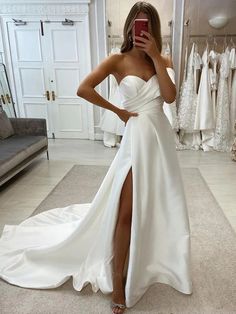 a woman taking a selfie while wearing a white wedding dress with high slits