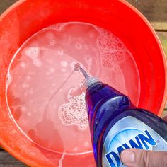 a hand is holding a bottle of detergent in front of a red bucket