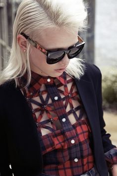 a woman with blonde hair and sunglasses looking at her cell phone while wearing a plaid shirt