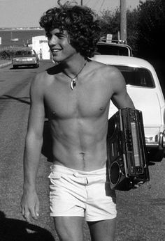 a shirtless young man walking down the street with an old radio in his hand