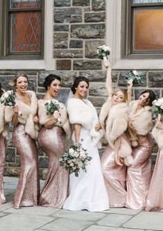 a group of women standing next to each other in front of a stone building with fur stoles