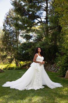 a woman in a wedding dress standing on the grass with her arms around her waist