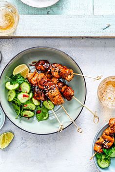 chicken skewers with cucumbers and salad on a plate next to two glasses of beer