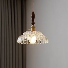 a glass light hanging from a ceiling in a room with curtains and drapes on the windowsill