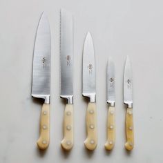 five knives are lined up next to each other on a white surface with yellow handles