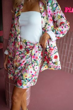 a woman standing in front of a pink wall wearing a floral print skirt and jacket