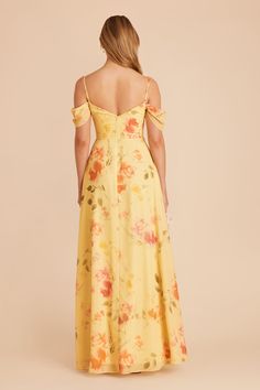 a woman in a yellow floral print dress with her back to the camera, looking down