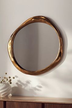 a round mirror sitting on top of a wooden table next to a vase with flowers