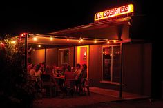 a group of people sitting at a table in front of a building with lights on it