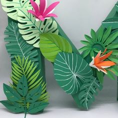 some paper flowers and green leaves on a white table top with the letter n in the middle