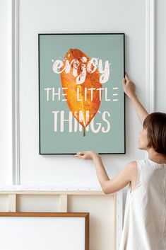 a woman is holding up a painting that says enjoy the little things