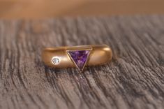 Signed Mid-century modernist ring bezel set with a trillion cut amethyst in the center. On one side of the amethyst is a flush set round brilliant cut diamond. The ring is finished with a sandblasted appearance and is signed "Sam Lena" or "Sam Lera".  This ring is currently a finger size 6, but can be adjusted to any size. Modern Amethyst Ring With Bezel Setting, Modern Purple Amethyst Ring For Anniversary, Modern Amethyst Ring For Wedding, Modern Amethyst Wedding Ring, Modernist Ring, Ring Bezel, Round Brilliant Cut Diamond, Brilliant Cut Diamond, Bezel Setting