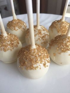 four white cake pops with gold sprinkles on them sitting on a plate