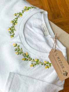 a white t - shirt with yellow flowers on it and a tag hanging from the front