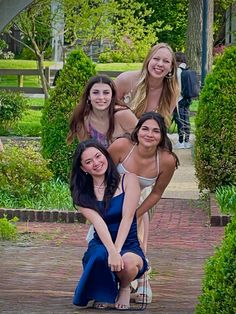 three women posing for a photo in front of some bushes and trees with one woman leaning on the ground