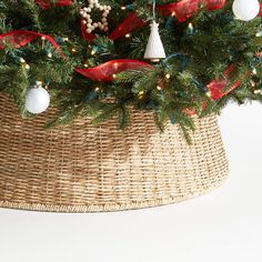 a christmas tree in a wicker basket with red and white ribbon on it's edge