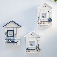 three white birdhouses are hanging on the wall next to each other with blue roof tops