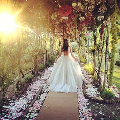 a woman in a wedding dress walking down a path with flowers all over the ground