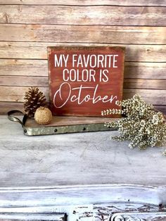 a wooden sign that says my favorite color is october next to some flowers and a pine cone