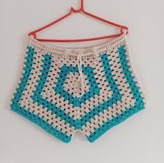 a crocheted blue and white shorts hanging on a hanger with a red hook