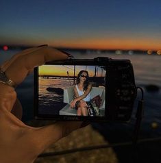 a person holding up a camera to take a photo with the sunset in the background