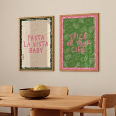 two posters on the wall above a table with a bowl of fruit in front of it