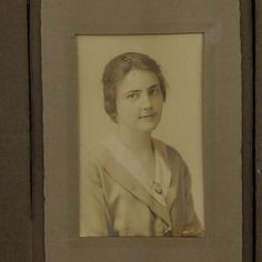 an old black and white photo of a woman in a dress with a sash around her neck