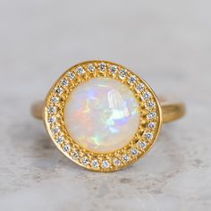 an opal and diamond ring sits on a marble surface, surrounded by small white diamonds