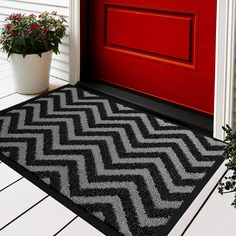 a red door with a black and gold door mat next to a potted plant