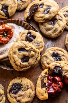 chocolate chip cookies are arranged on a wooden table next to a bowl of cherries