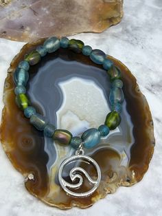 This beautiful OOAK sea glass stretch bracelet is made with gorgeous green and blue sea glass, frosted glass & a beautiful silver wave 🌊charm dangle.  It measures 7 inches in length on 100% polyester stretch cord, not wire. It's the perfect summer accessory. Bohemian Green Crystal Bracelet For Beach, Adjustable Czech Glass Bracelets For Beach, Blue Spiritual Stretch Bracelet For Beach, Spiritual Blue Stretch Bracelet For Beach, Czech Glass Beaded Bracelets For Beach, Czech Glass Round Bead Bracelets For The Beach, Blue Czech Glass Bracelets For Beach, Green Crystal Bracelet With Round Beads For Beach, Blue Czech Glass Bracelet For Beach