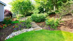 a garden with lots of green grass and flowers on the side of the house,