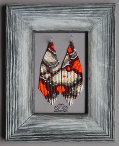 two red and white beaded earrings hanging from a gray framed photo in a wooden frame