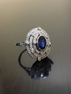 DeKara Designs CollectionArt Deco Inspired Extremely Elegant Halo Sapphire Diamond Engagement Ring.Metal- 90% Platinum, 10% Iridium.Stones- 1 Oval Ceylon Blue Sapphire 1.25 Carats, 100 Round Diamonds F-G Color VS2 Clarity .80 Carats.  Size- 6 1/4.An Amazing Art Deco Inspired Ceylon Blue Sapphire Triple Halo Diamond Engagement.  The ring features a beautiful Ceylon Blue Sapphire that is expertly bezel set in the center.  The sapphire is surrounded by 92 pave and burnish set round sparkling diamon Luxury Sapphire-colored Diamond Ring With Diamond Cut, Luxury Sapphire-colored Diamond Ring, Luxury Sapphire Baguette Cut Ring, Luxury Sapphire Diamond Ring With Diamond Cut, Luxury Sapphire Platinum Rings, Luxury Sapphire Diamond Ring With Center Stone, Luxury Platinum Topaz Ring With Halo Setting, Platinum Oval Halo Ring With Gemstone, Oval Platinum Halo Ring With Gemstone