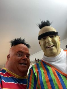 two men with fake hair are standing next to each other, one is wearing a striped shirt and the other has black mohawks on his head