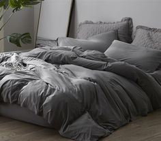 an unmade bed in a bedroom with grey sheets and pillows on the floor next to a potted plant